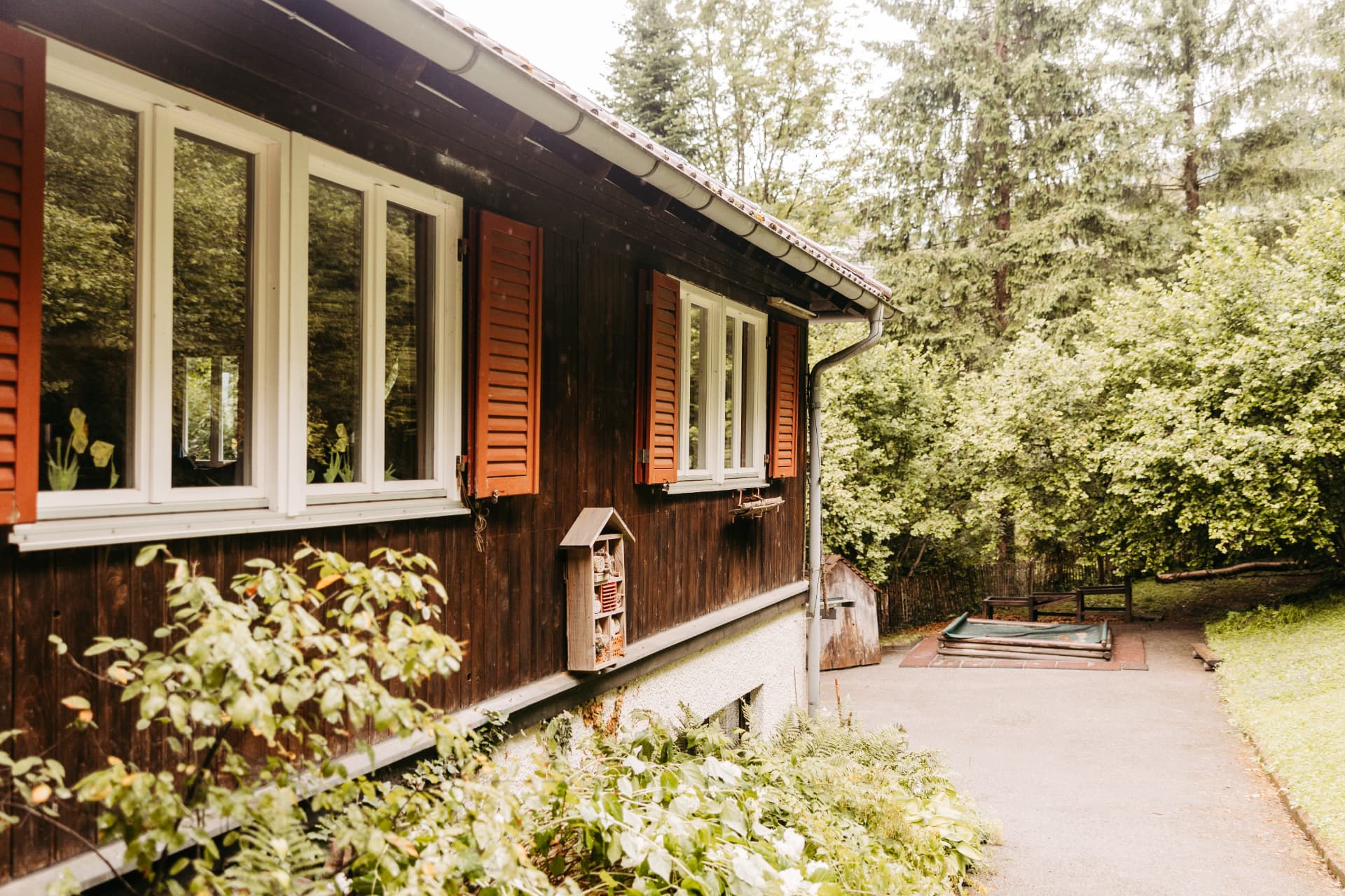 Holzhaus mit weissen Fenstern und roten Läden, eingebettet in Bäume